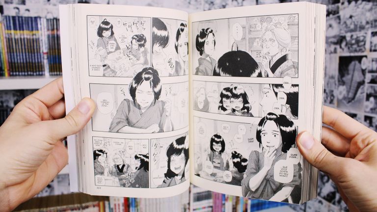 Imagem: Duas mãos seguram páginas abertas do mangá A Lanterna de Nix, com páginas em preto e branco.