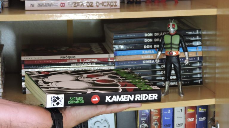 Imagem: Lombada do mangá e boneco do Kamen Rider.