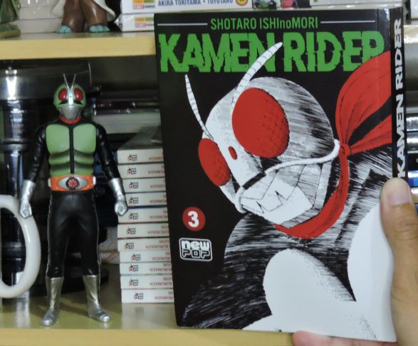 Imagem: Capa do volume 3 de 'Kamen Rider' ao lado de boneco do personagem.