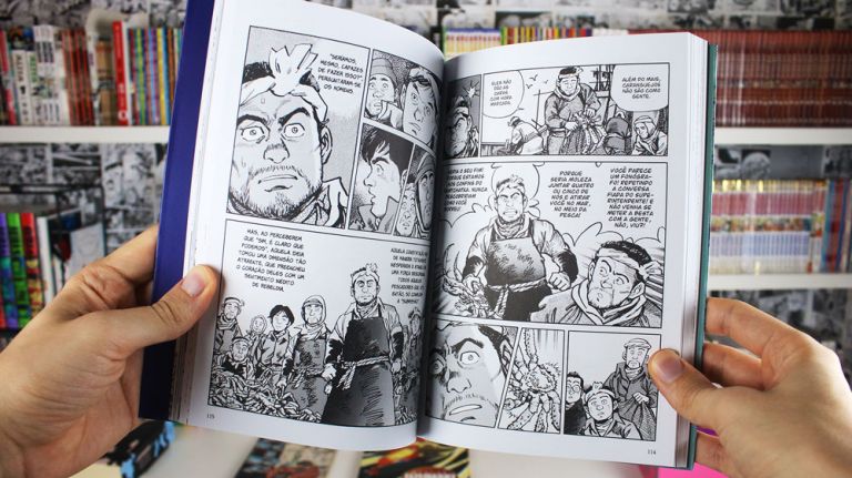 Imagem: Foto de mão segurando o Kanikosen mostrando páginas da história, ao fundo uma estante cheia de livros e mangá.