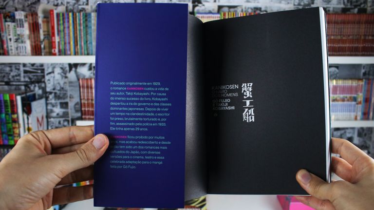 Imagem: Foto de mão abrindo a última página e mostrando a contracapa traseira de Kanikosen, ao fundo uma estante cheia de livros e mangá.